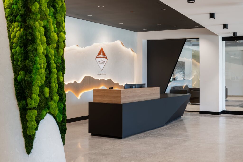 Modern reception area for The Miller Group featuring a custom-lit topographical wall graphic and a pillar wrapped in lush preserved green moss.