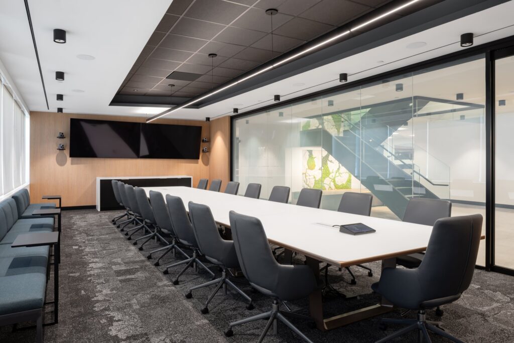 A long executive boardroom featuring wood paneling, integrated technology, and a clear glass wall overlooking architectural office graphics.