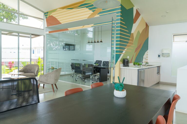 Abstract geometric landscape wall graphic in earthy tones wrapping around a glass-enclosed meeting room and office kitchenette.