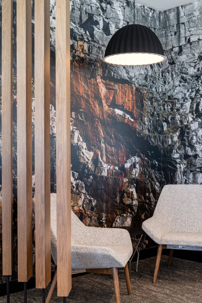 A high-impact photographic wall mural of a granite rock face installed in a corporate lounge behind modern grey armchairs.