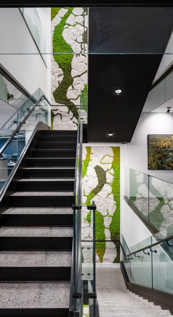 A dramatic vertical installation of preserved biophilic moss and white rock textures spanning multiple floors alongside a modern black office staircase.