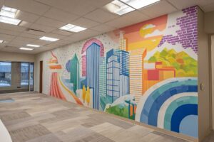 A full-length stylized cityscape wall mural using bright geometric shapes to transform a vacant commercial office space.